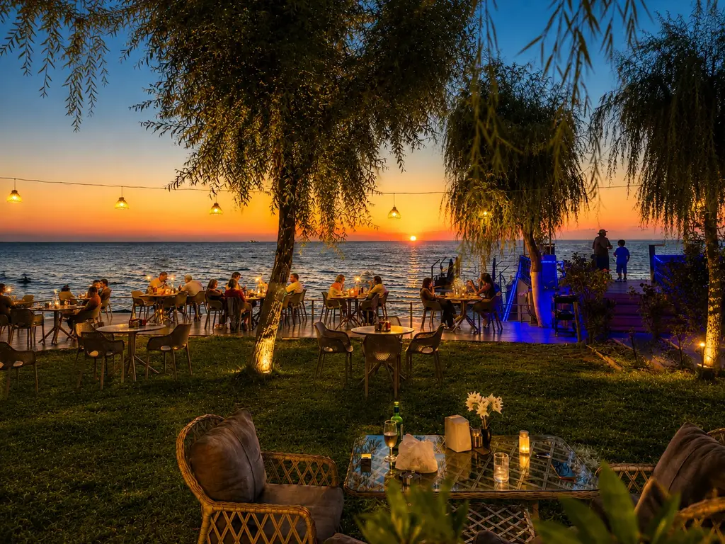 Restoran bahçesinde gün batımında masalar, arkada deniz